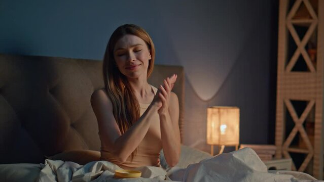 Girl moisturizing arms skin at bedtime home. Happy woman applying cream on hands