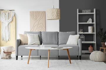 Stylish interior of living room with grey sofa, coffee table and shelving unit