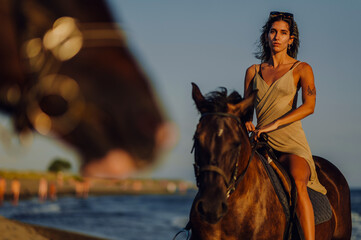Gorgeous woman looking at the camera while riding horse on the beach