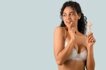 Young African-American woman with vibrator on light background