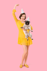 Young woman and cute pug dog in party hats on pink background