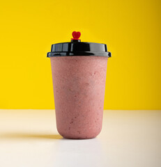 A glass of blueberry milkshake in yellow background