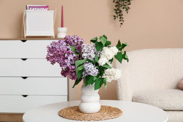 Vase with lilacs branches on coffee table in stylish living room