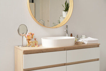 Mirror, decorative cosmetics, towels and bottles for skincare on chest of drawers in bathroom