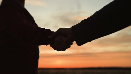 Handshake at sunset, silhouette in park field. At dawn in agricultural field women make deal agree on joint cooperation. Shaking hands gesture close business friendship. Strong long joyful handshake.