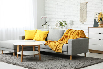 Interior of light living room with comfortable sofa, cushions and yellow plaid