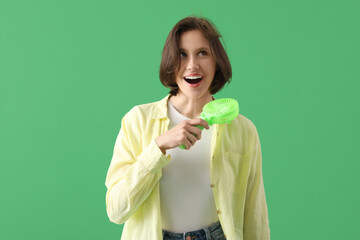 Young woman with portable electric fan on green background