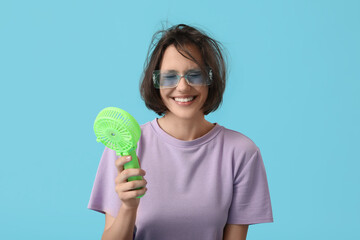 Young woman with green small electric fan on blue background
