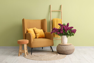 Armchair, ladder and lilac flowers in vase on pouf in living room