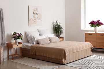 Bedroom with large bed and lilac flowers in vase on chest of drawers