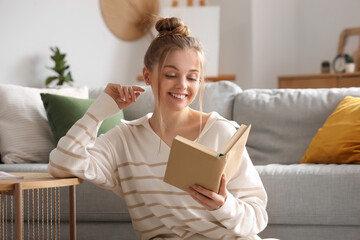 Young woman reading book near sofa in living room
