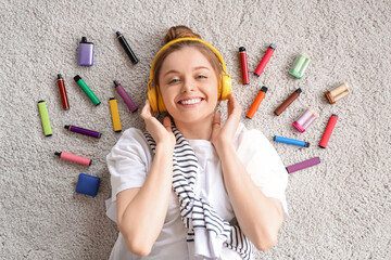 Young woman in headphones lying on floor near different disposable electronic cigarettes at home