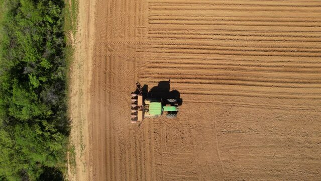 Aerial tracking high angle shot of tractor seeding a field with a seed drill in the mountains on a sunny spring day. Planter towed by a machine along a rural farmland. Ecologic farming concept.

