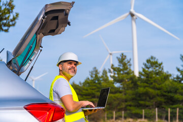Engineer controlling wind turbines using laptop in an energy park