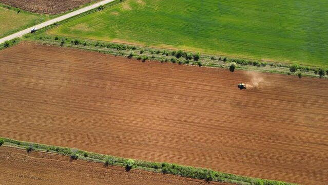 Aerial tracking high angle shot of tractor seeding a field with a seed drill in the mountains on a sunny spring day. Planter towed by a machine along a rural farmland. Ecologic farming concept.
