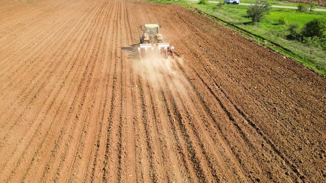 Aerial tracking high angle shot of tractor seeding a field with a seed drill in the mountains on a sunny spring day. Planter towed by a machine along a rural farmland. Ecologic farming concept.
