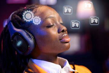 African american woman at home closing eyes, using futuristic headphones and AR technology to...