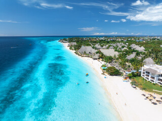 Aerial view of white sandy beach, blue sea, bungalows, green palms, umbrellas, boats at sunset. Summer travel in Nungwi, Zanzibar island. Tropical landscape. Top drone view of luxury resort. Ocean