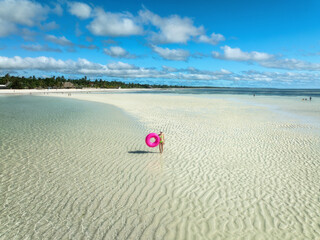 Aerial view of sporty slim woman with swimming ring, sandy beach, blue sea during low tide at sunny summer day in Zanzibar island. Top view of beautiful girl, sandbank, ocean, sky with clouds, palms