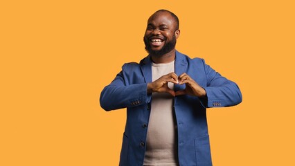 Portrait of jolly friendly african american man doing heart symbol shape gesture with hands....