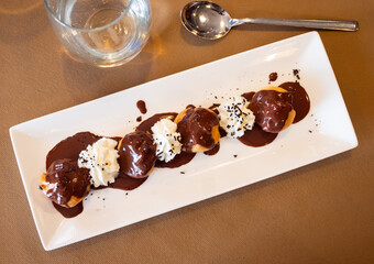 Top view of delicate profiteroles topped with chocolate glaze on plate. Traditional baked French...