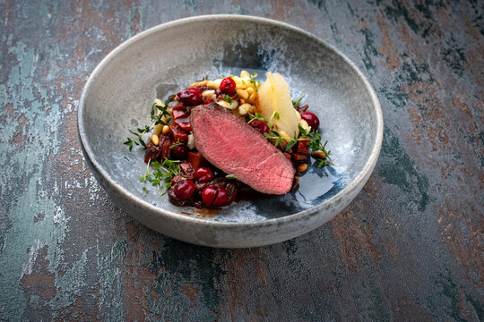 Traditionell gebratener Rehr&uuml;cken mit S&uuml;dtiroler mit Sp&auml;tzle, Gem&uuml;se und Obst in Schokoladen Rotwein Sauce serviert als Nahaufnahme auf einem Nordic Design Teller mit Textfreiraum