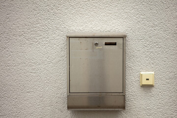 A mailbox on a house wall. Metal, plaster, exterior. 
