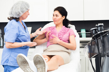 Fototapeta premium Highly qualified cosmetology doctor working in the clinic tells a young female patient sitting on a couch about the ..health of the female breast, explaining how to properly care for it to maintain a