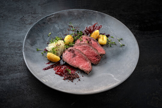 Traditional fried venison back filet with sliced pear, gnocchi and plum jam served as close-up on Nordic design plate