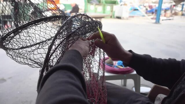 Fisherman Repairs Fish Catching Basket Net with Net Repair Needle Footage.