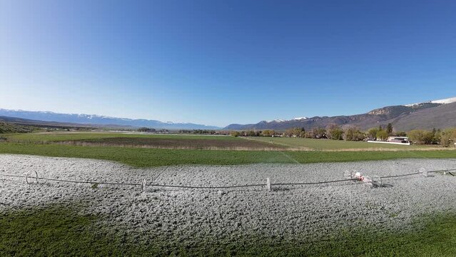 Aerial crossing alfalfa field ice irrigation spr. rural agriculture farming community economy. Irrigation water in wheel lines. Early Spring season cool cold weather mountain valley agriculture field.