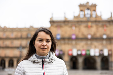Smiling adult female tourist enjoying walking in ancient Spanish city of Salamanca on spring day,...