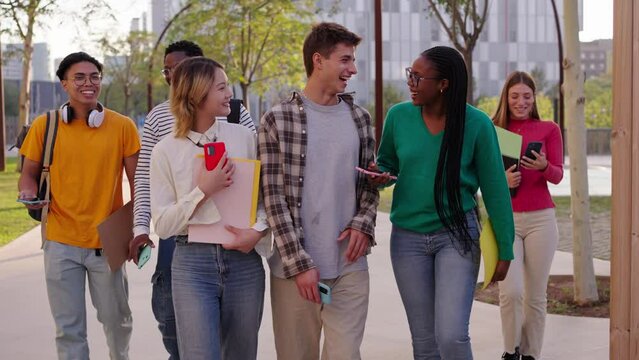 Group of multicultural students standing walking together outside the university campus building. Young diverse friends smiling and looking at each other with backpacks and workbooks outdoor