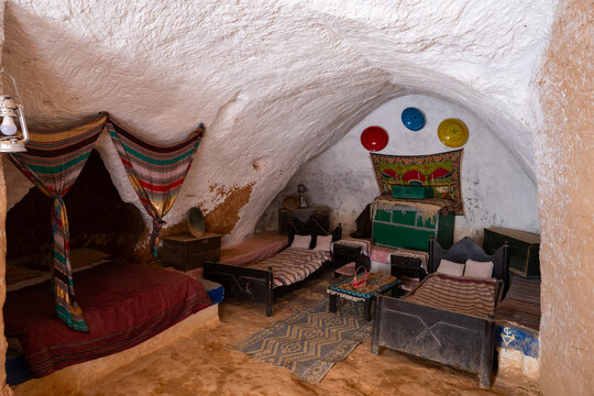 Simple cozy Berber bedroom in Matmata cave dwelling with double bed for parents and two wooden beds for kids, traditional colorful textiles and decorations, reflecting troglodyte lifestyle of Tunisia