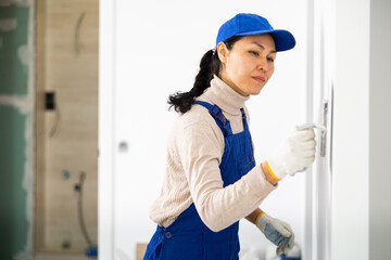Asian woman repairer applying plaster to a wall with floated trowel.