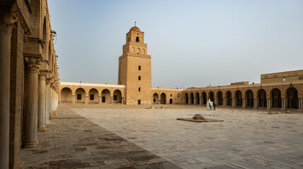 Naklejka premium Courtyard patio of ancient grand mosque of Kairouan in Tunisia, view of minaret. Religious Islamic building, place of worship and prayer for many generations of Muslims