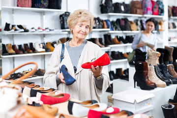 Granny choosing new shoes while standing in salesroom of shoeshop. - obrazy, fototapety, plakaty