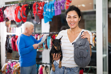 Asian woman choosing winter clothes for her doberman pinscher dog at pet store