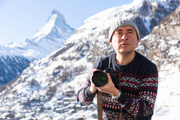 Travel photographer with camera taking pictures of mountain landscape of Swiss Alps on sunny winter...