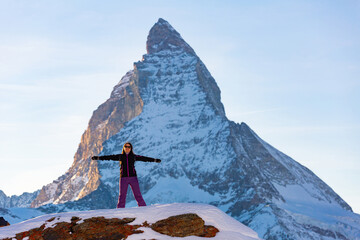 Happy young woman in ski suit posing outdoors on background of high pyramidal snow-capped...