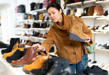 Asian woman choosing new boots in shoe store.