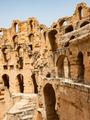 Naklejka premium Scenic view of time weathered honey-colored limestone walls of antique Roman amphitheater in Tunisian city of El Djem, with surviving arched openings basking in warm sunlight..