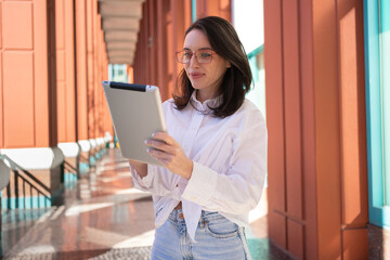 Businesswoman in glasses using digital tablet, standing outdoor. Female freelancer holding tablet...