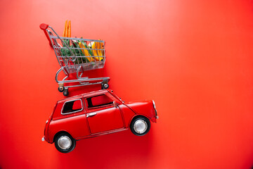Delivery of products. Red car with a shopping basket on the roof with fruits and vegetables on a...