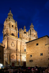 Naklejka premium Scenic Salamanca cityscape at spring twilight with busy central square, illuminated medieval building of Casa de las Conchas decorated with stucco shells and baroque building of La Clerecia, Spain