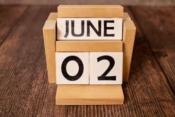 Cube shape calendar for June 02 on wooden surface with empty space for text.