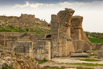 Obraz premium Scenic view of Licinius Sura Baths, well-preserved Roman ruins in Dougga, surrounded by spring greenery in Tunisia against cloudy backdrop