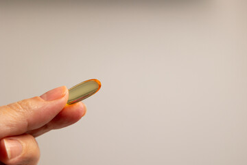 woman's hand holding a pill of fish oil with omega 3 with a golden yellow color, an essential...