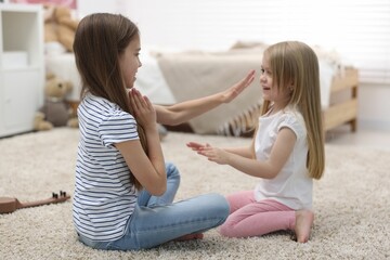 Cute little sisters playing clapping game with hands at home
