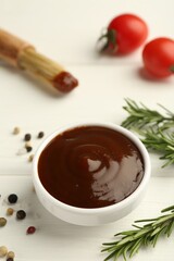 Tasty barbeque sauce in bowl, rosemary and spices on white wooden table